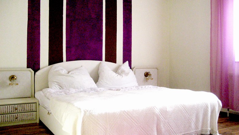 Schlafzimmer mit weißem Bett und lila Streifen an der Wand.