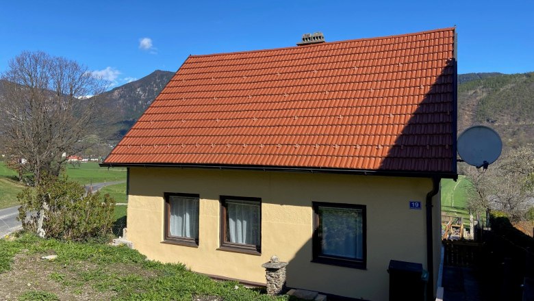 Kleines gelbes Haus mit rotem Dach in ländlicher Umgebung.