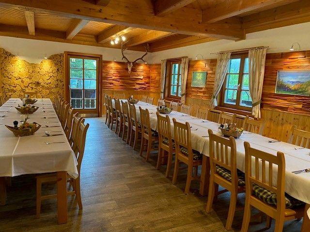 Rustikaler Speisesaal mit langen, gedeckten Tischen und Holzwänden.