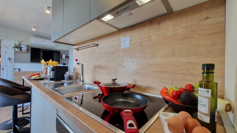 Modern kitchen with pans, vegetables, eggs and oil bottle on the worktop.