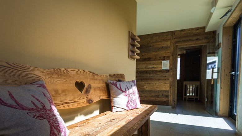 Rustic wooden bench with heart motif and deer cushions in a sunny room with wooden walls.