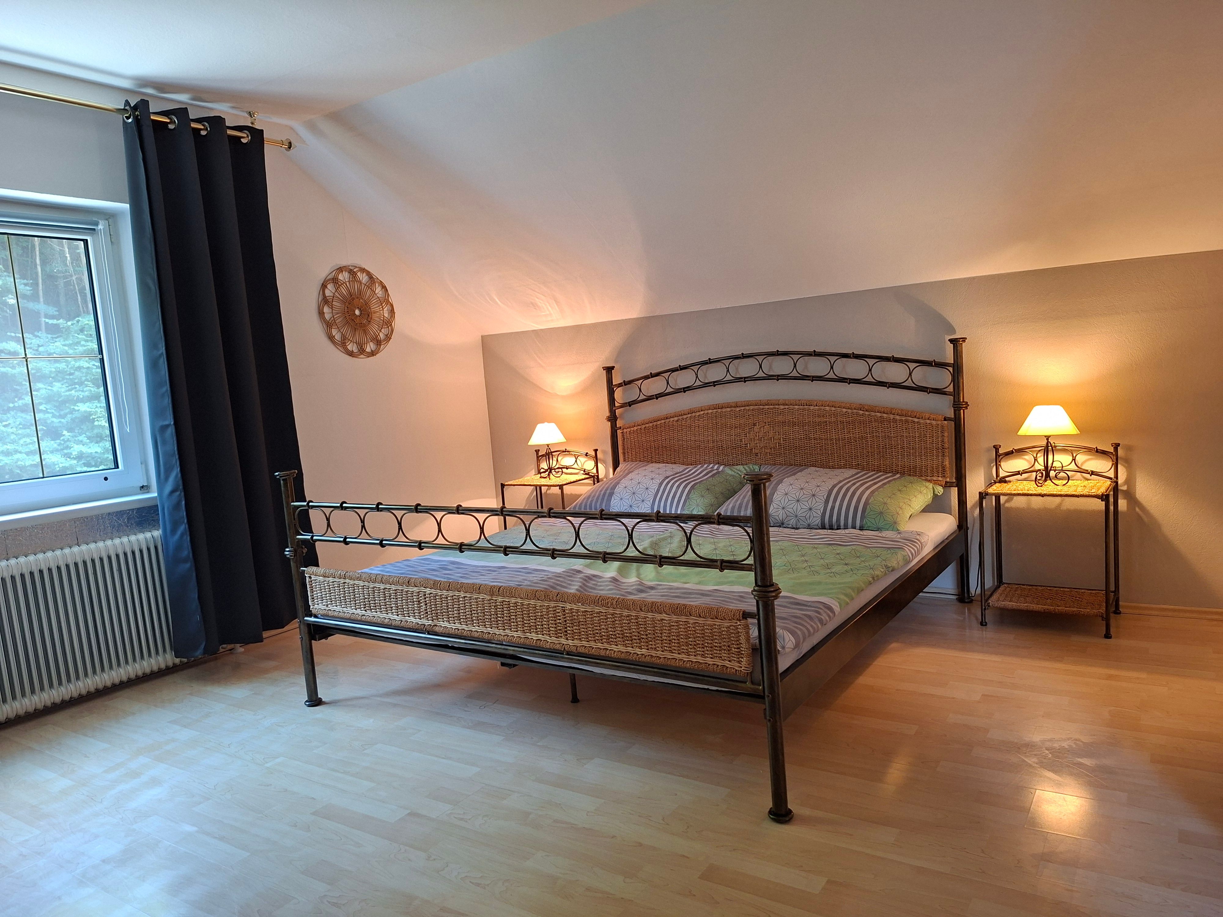 Ein gemütliches Schlafzimmer mit einem Metallbett, zwei Nachttischen mit Lampen und einem Fenster mit dunklen Vorhängen.