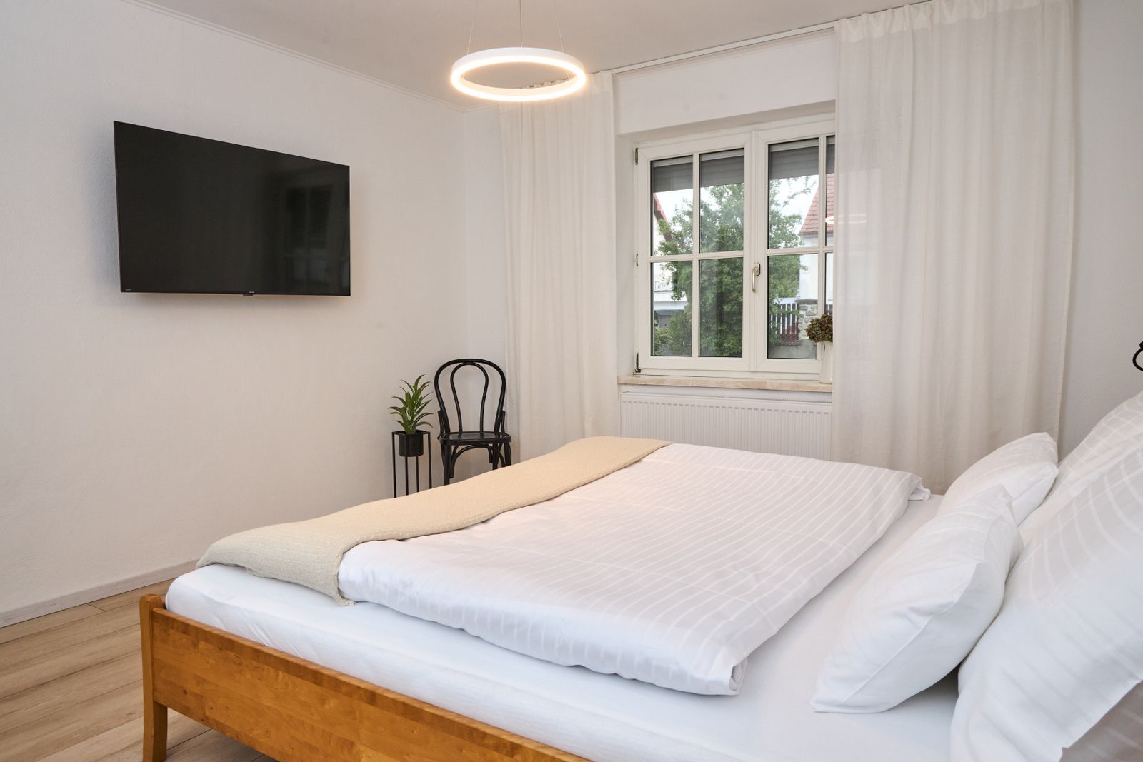 Bright bedroom with double bed, window, TV and chair.