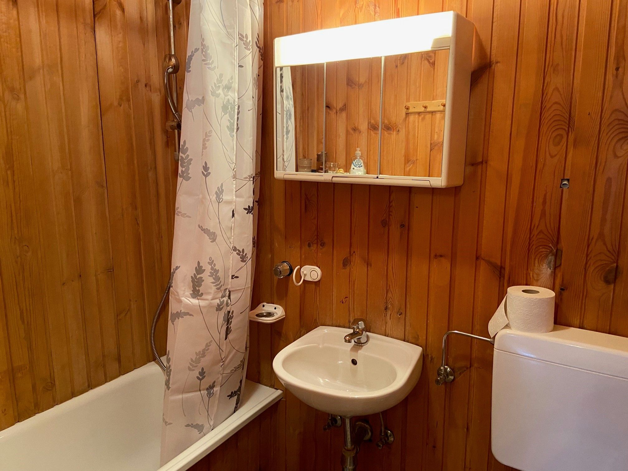 Holzvertäfeltes Badezimmer mit Badewanne, Duschvorhang, Waschbecken und Spiegelschrank.