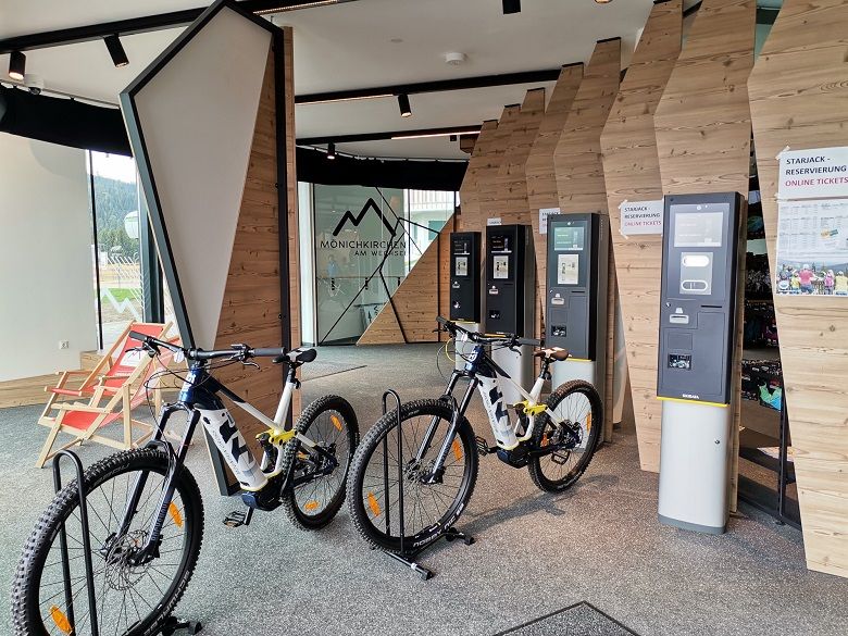 Innenansicht eines E-MTB Verleihs mit Fahrrädern und Ticketautomaten.