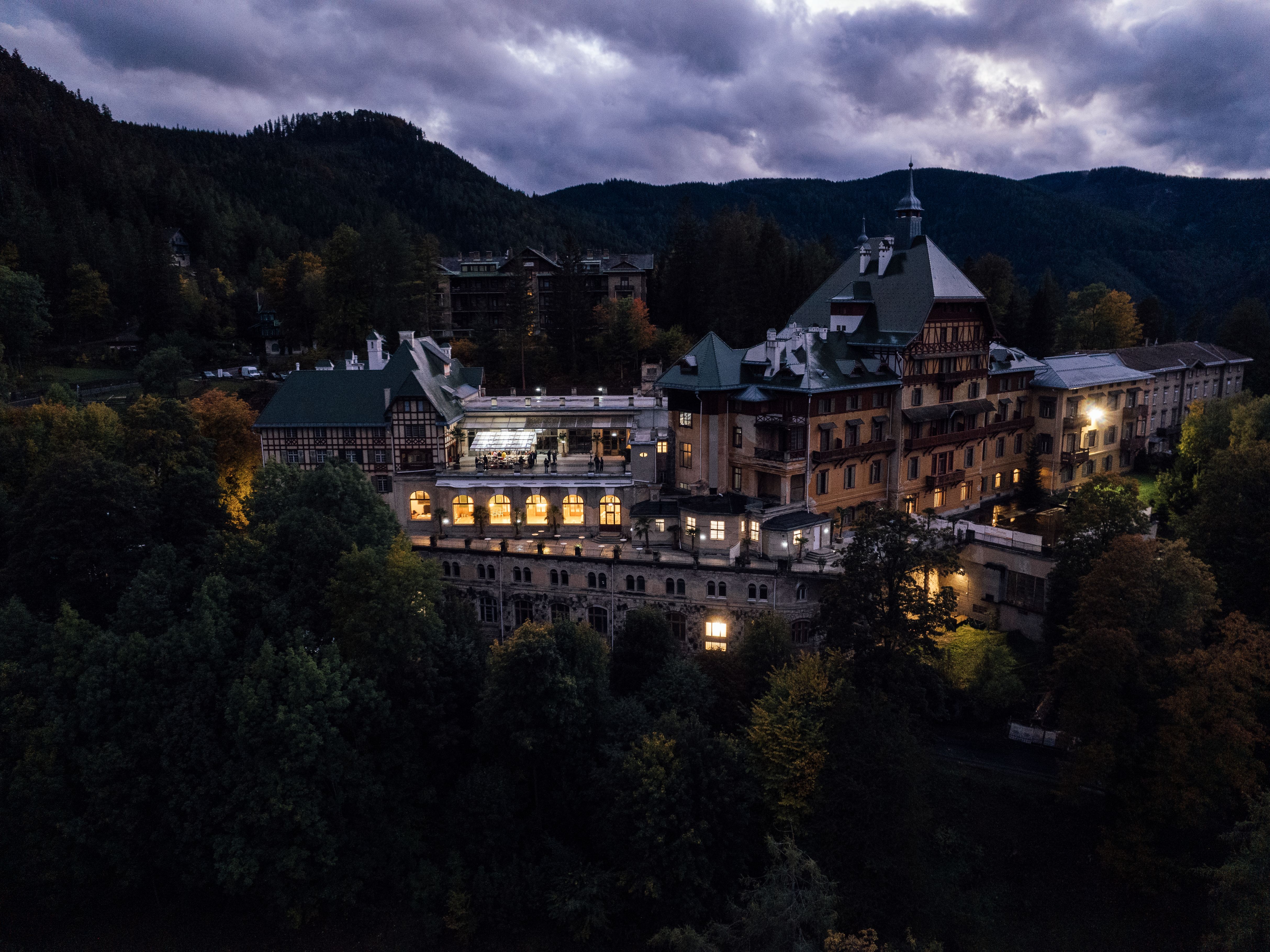 Inmitten der majestätischen Wiener Alpen erstrahlt das historische Gebäude in warmem Licht, umgeben von der bunten Pracht des herbstlichen Laubs. Die sanften Hügel und die dramatische Wolkenkulisse schaffen eine Atmosphäre der Ruhe und Erholung, die zum Verweilen einlädt.