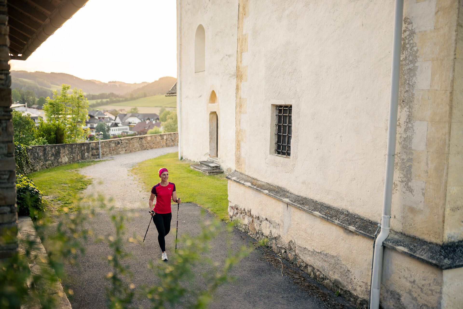 Eine Frau in Sportbekleidung geht mit Walkingstöcken bei der Wehrkirche Bad Schönau vorbei.