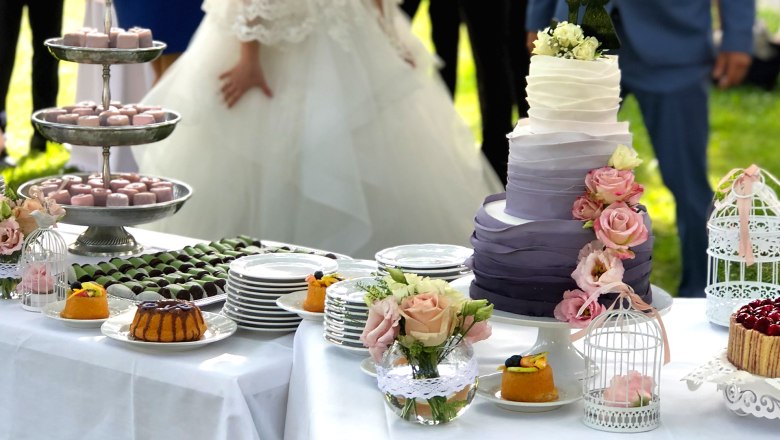Wedding cake and desserts on an outdoor table with the bride and groom.