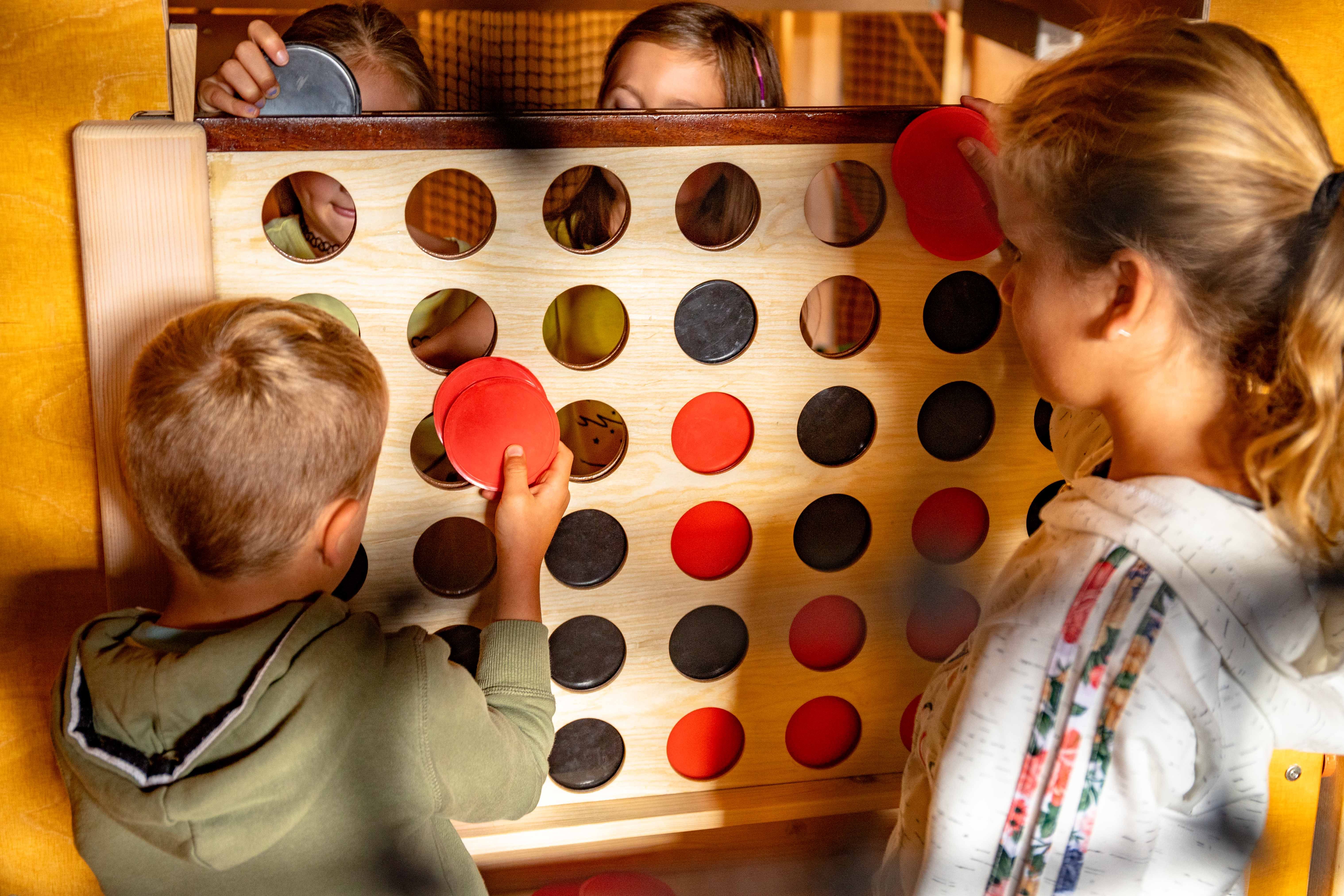Kinder spielen ein großes Vier-Gewinnt-Spiel mit roten und schwarzen Scheiben.