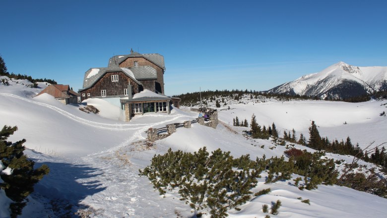 Winterlandschaft mit dem Ottohaus und schneebedeckten Bergen im Hintergrund.