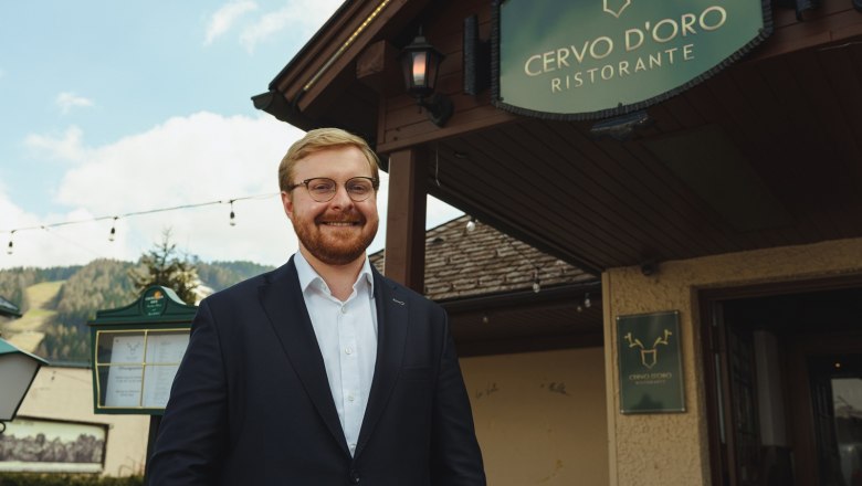 A man in a suit stands smiling in front of the Cervo D'Oro restaurant.
