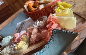 Eine rustikale Jause mit Wurst, K&auml;se, Brot und Aufstrichen auf einem Holzteller.