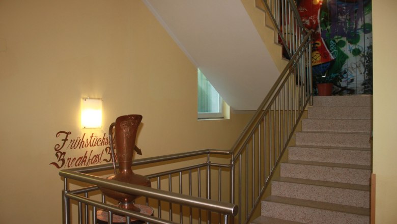 Staircase with banister, wall decoration and vase.