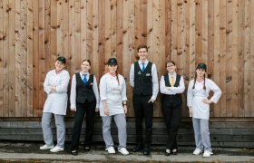 Sechs junge Menschen in Uniformen vor einer Holzwand.
