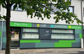 Exterior view of a caf&eacute; with green fa&ccedil;ade and tree in the foreground.