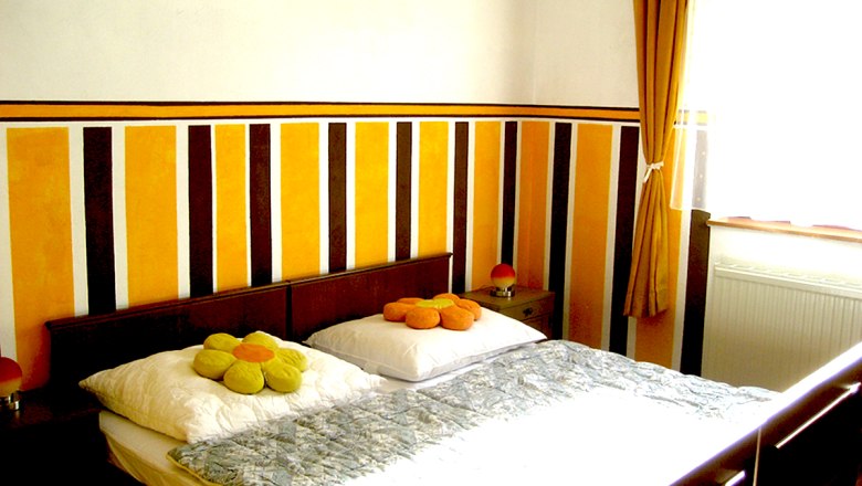 Ein Schlafzimmer mit einem Doppelbett, gestreifter Wand und gelben Vorhängen.