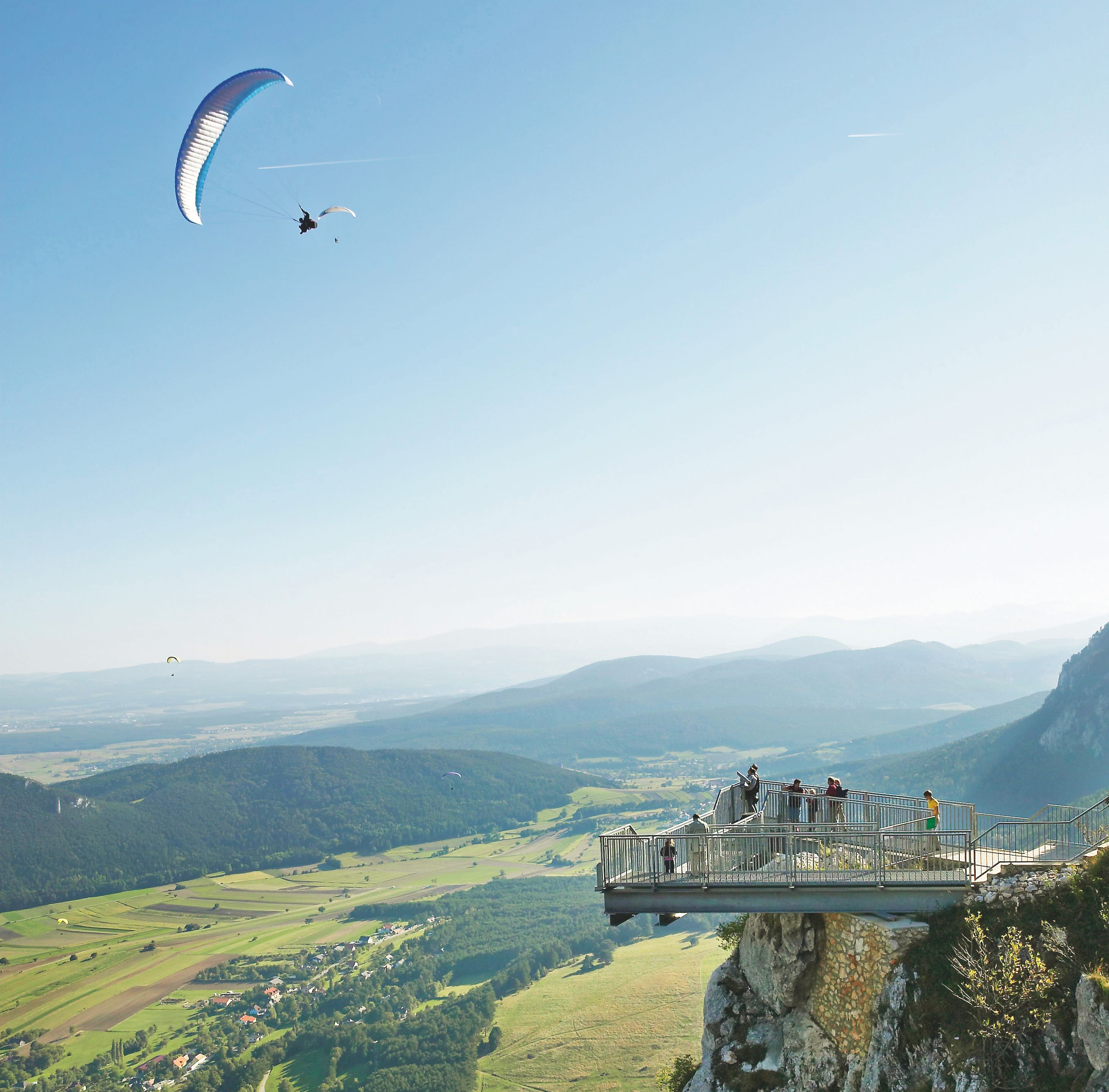 Eine Person geht auf einem Skywalk über einem Nebelmeer in den Sonnenuntergang.