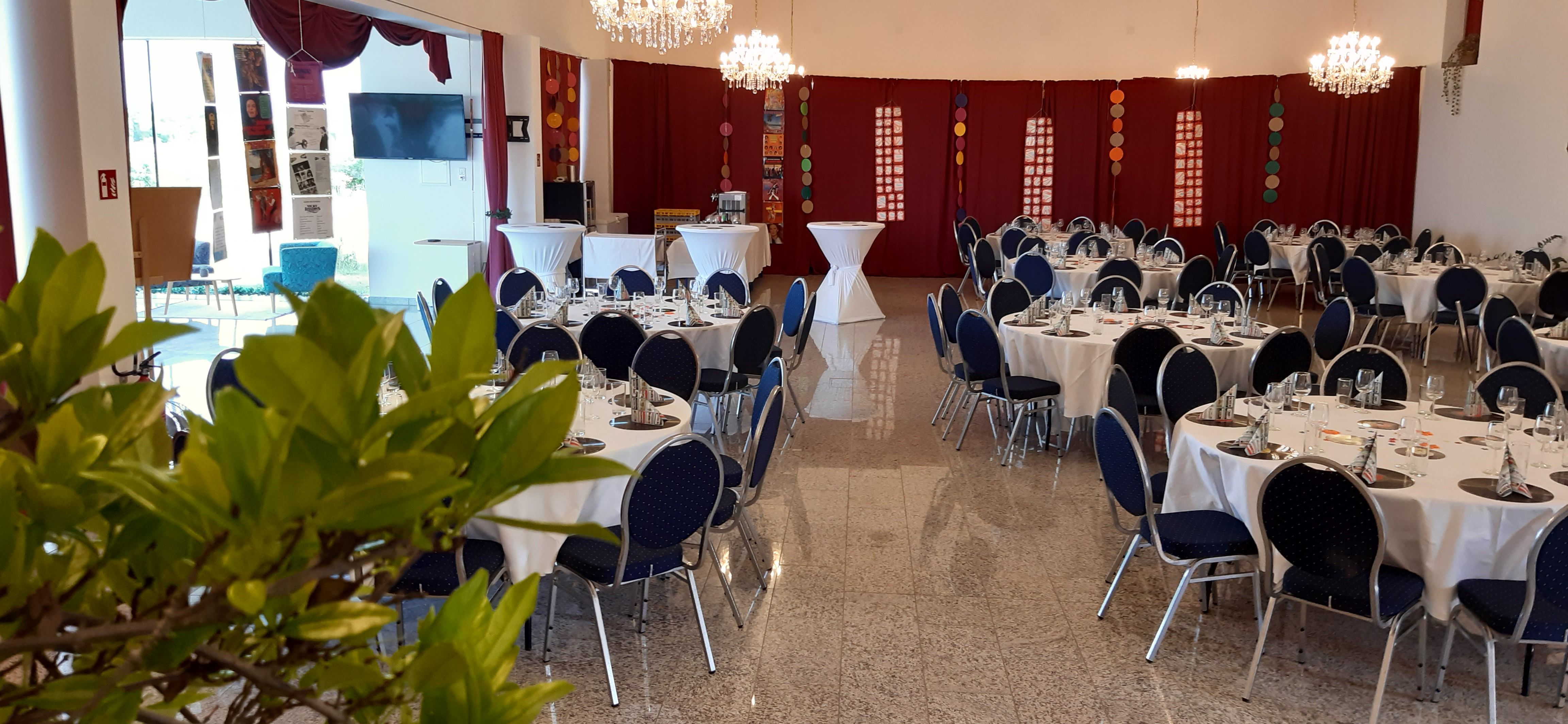 Saal mit runden Tischen und Stehtischen, sowie roten Raumelementen