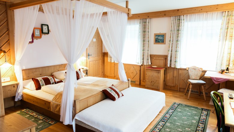 Gemütliches Hotelzimmer mit Himmelbett, Holzmöbeln und Teppichen.