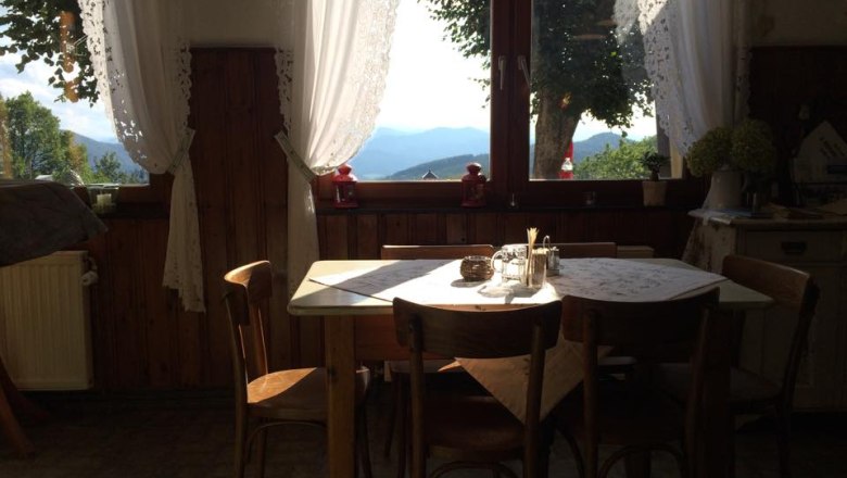 Ein gemütlicher Essbereich mit Holztisch und Stühlen vor einem großen Fenster mit Blick auf Berge und Bäume.
