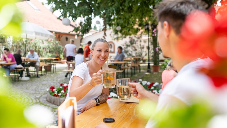 Personen stoßen mit Getränken im Freien an, umgeben von Bäumen und Blumen.