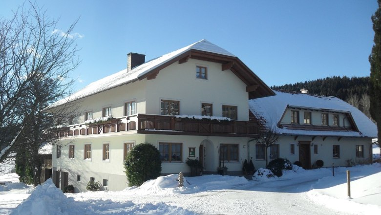 unser Hof im Winter, © Familie Rosinger Ein großes Bauernhaus im Winter mit Schnee bedeckt, unter blauem Himmel.