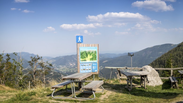 Picknicktische und Wanderschild mit Bergblick bei der Edelweißhütte am Schneeberg.