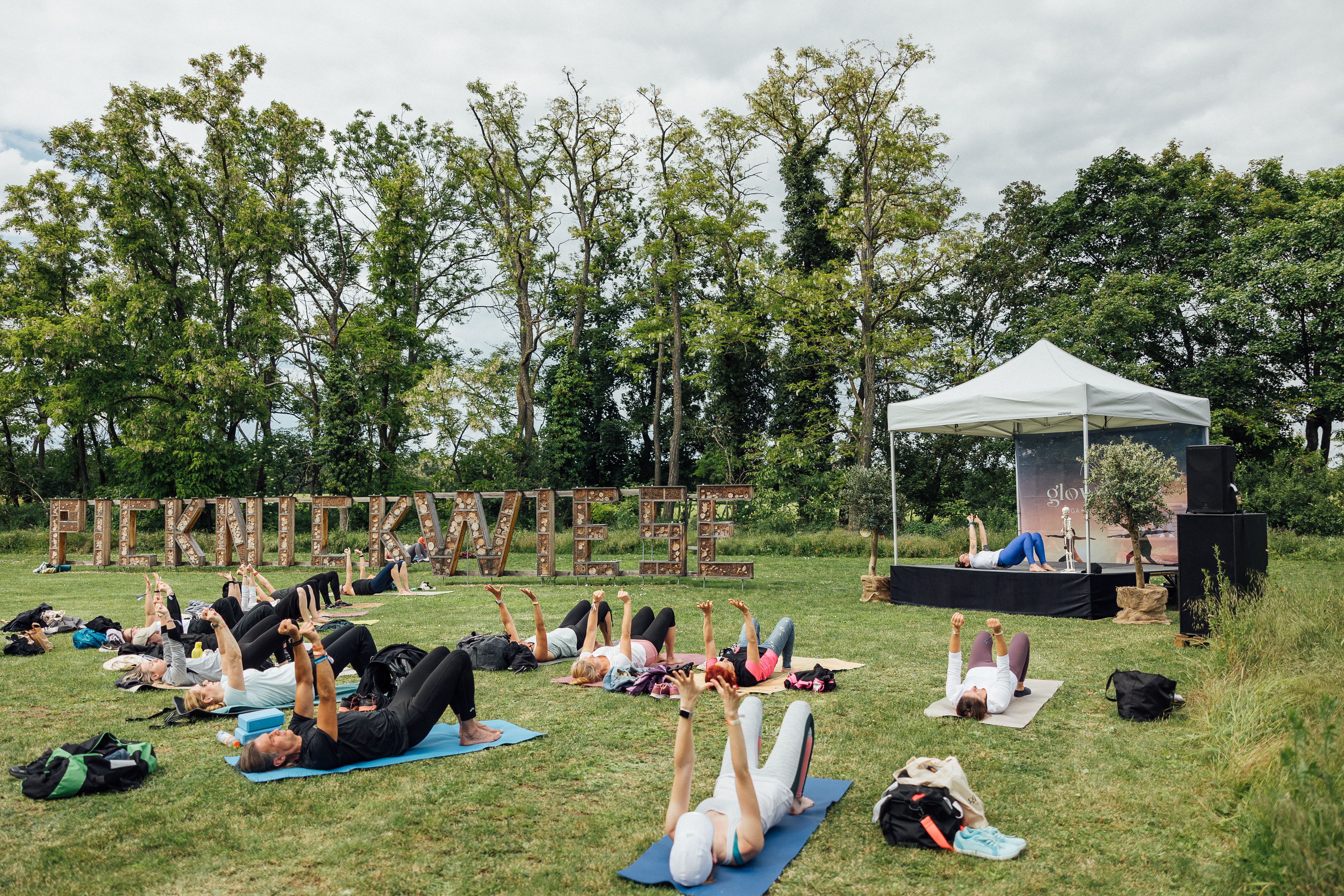 Große Wiese, auf der Personen vor einer Bühne Yogaübungen ausführen