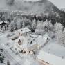 Snow-covered town with houses and trees, surrounded by mountains.