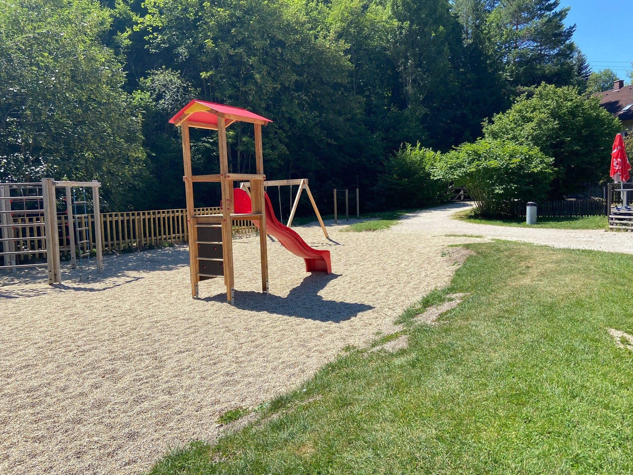 Ein Kinderspielplatz mit Rutsche und Klettergerüst, umgeben von Bäumen und Rasen.