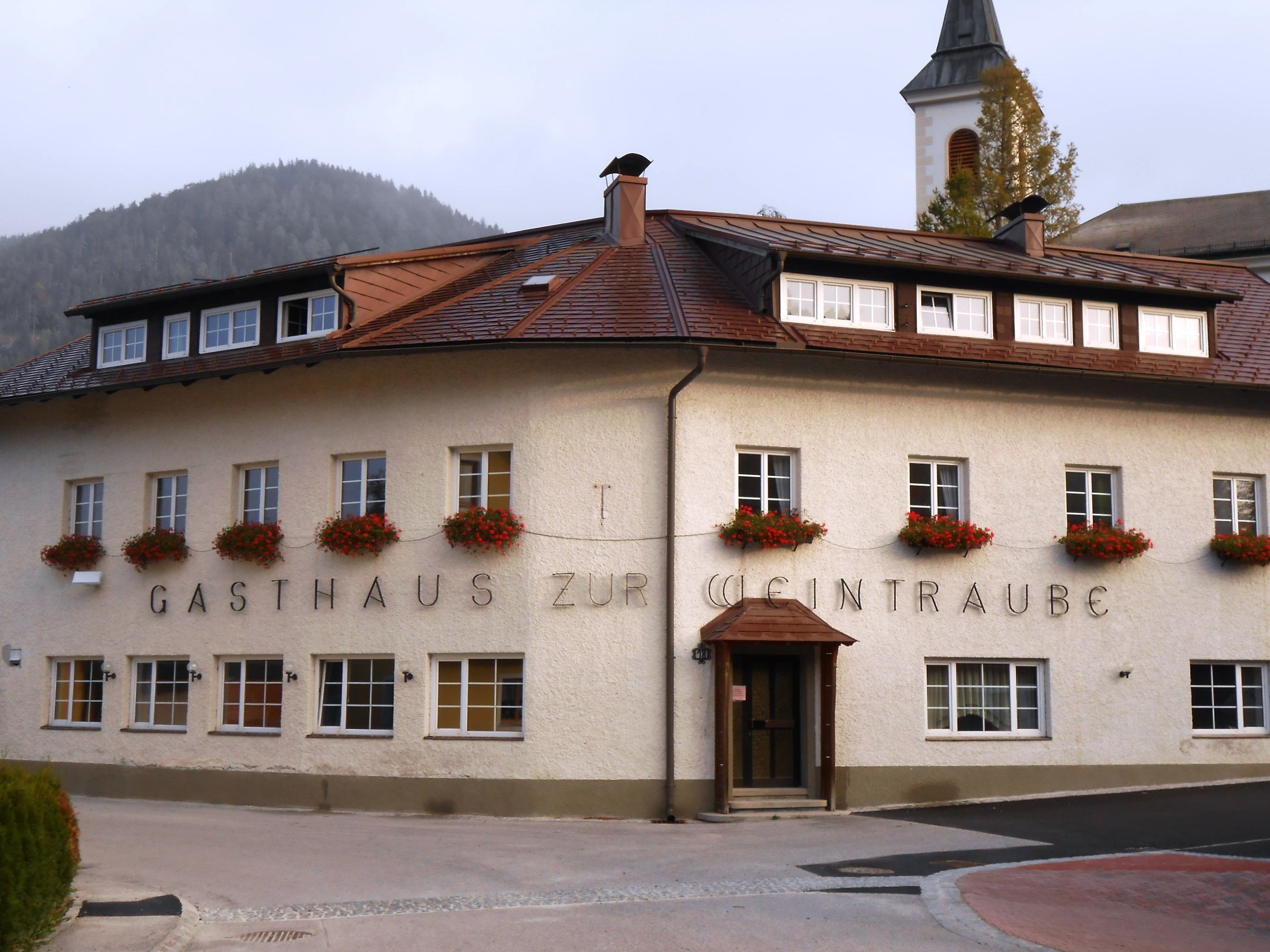 Ein traditionelles Gasthaus mit Blumen an den Fenstern und einem Kirchturm im Hintergrund.