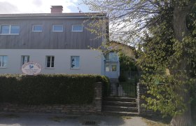 Zweist&ouml;ckiges Geb&auml;ude mit Schild 'Alpengasthaus Ewin' und Garten.