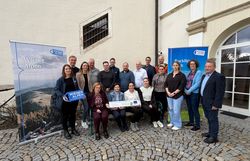 Mehrere Personen stehen in einem Innenhof und halten ein Wiener Alpen Schild und ein LEADER-Schild in den Händen.