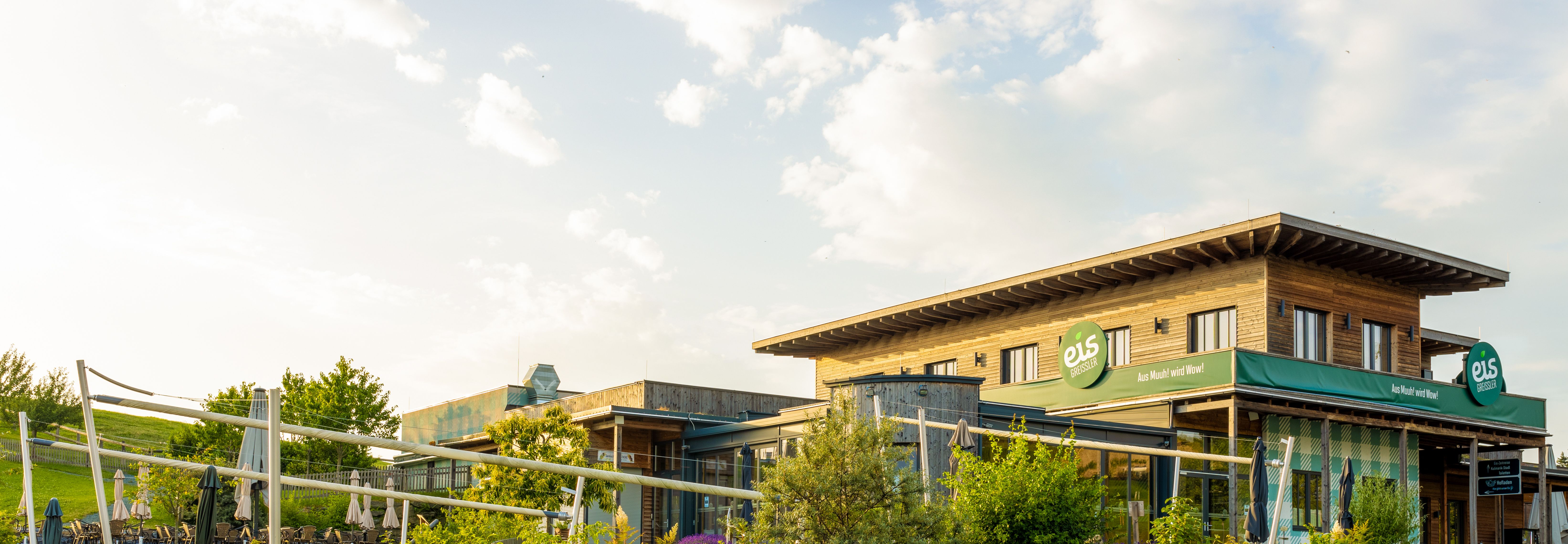 Außenansicht eines Holzgebäudes mit großer Grünfläche, Sonnenschirmen und einem Holzzaun.