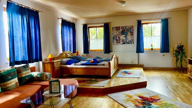 Gemütliches Zimmer mit Holzboden, Doppelbett, Sofa und blauen Vorhängen.