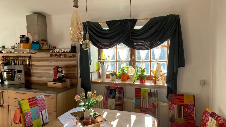 Essbereich mit Holztisch, bunten Stühlen, Pflanzen auf der Fensterbank und Hängelampen.