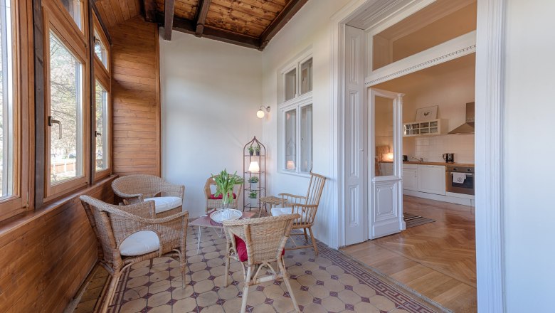 Wintergarten mit Holzwänden, Rattanmöbeln und Blick in eine Küche.