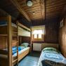 Wood-paneled triple room with bunk bed and single bed, window with curtain, rustic furnishings.