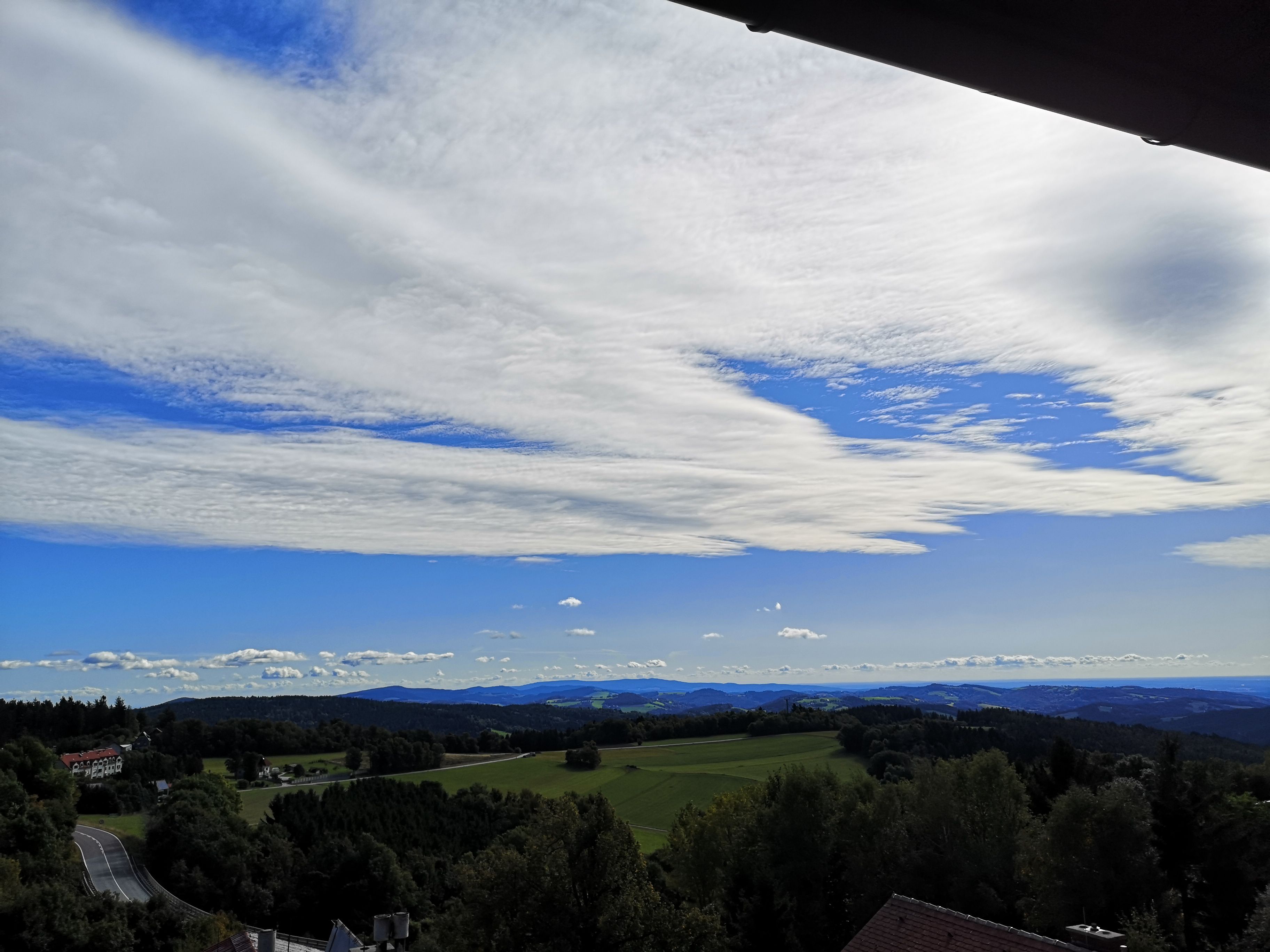 Landschaft mit Hügeln, Wäldern und weitem Himmel mit Wolken.