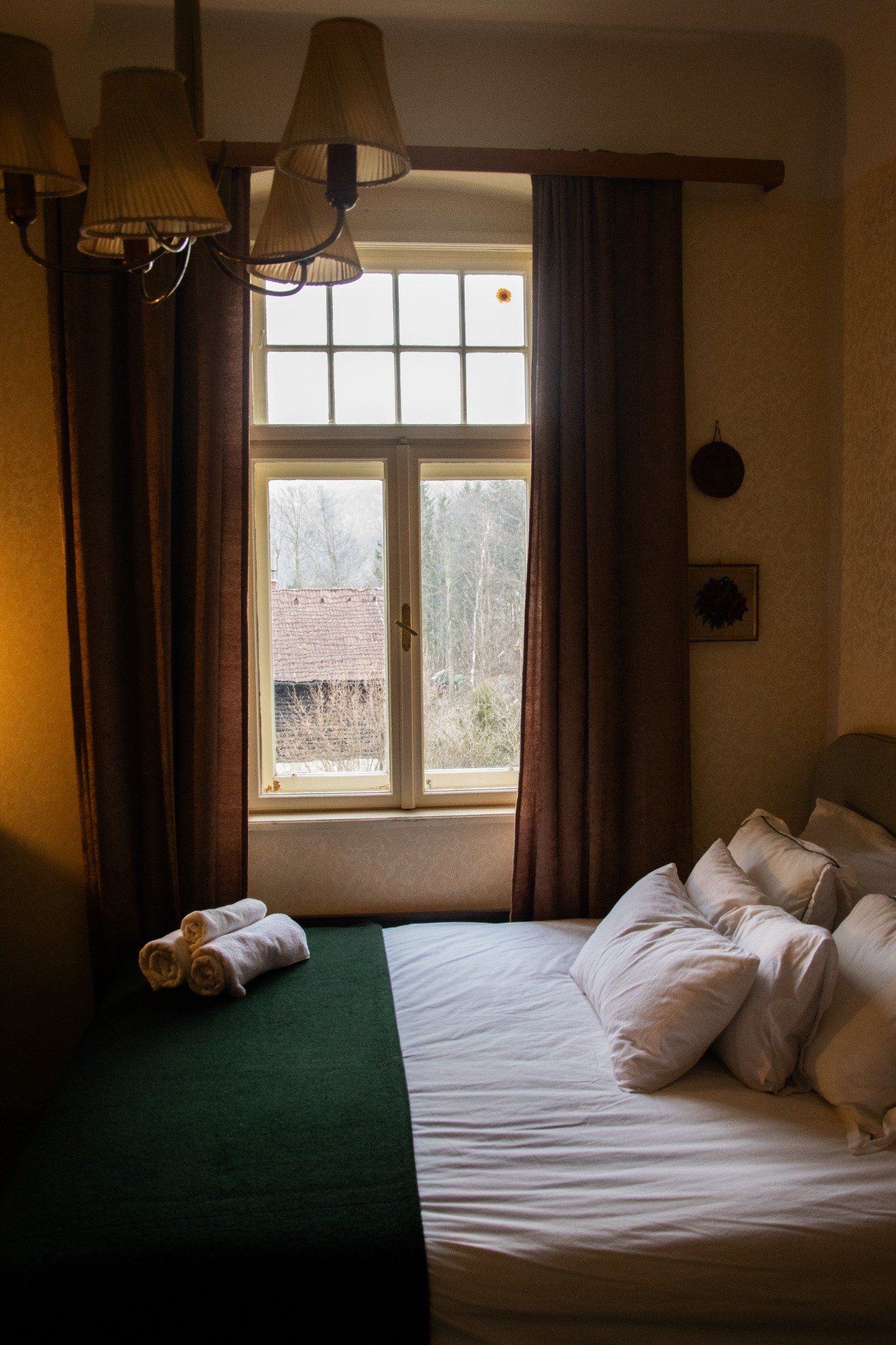 Ein gemütliches Schlafzimmer mit einem Bett, das vor einem Fenster steht. Draußen sind Bäume und ein Hausdach zu sehen.