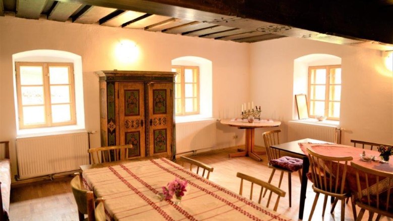 Gemütliche Stube mit Holzmöbeln, Tischdecken und einem bemalten Schrank.