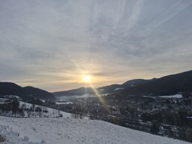 Winterlandschaft in Payerbach mit Sonnenaufgang &uuml;ber schneebedeckten H&uuml;geln und einem Dorf im Tal.