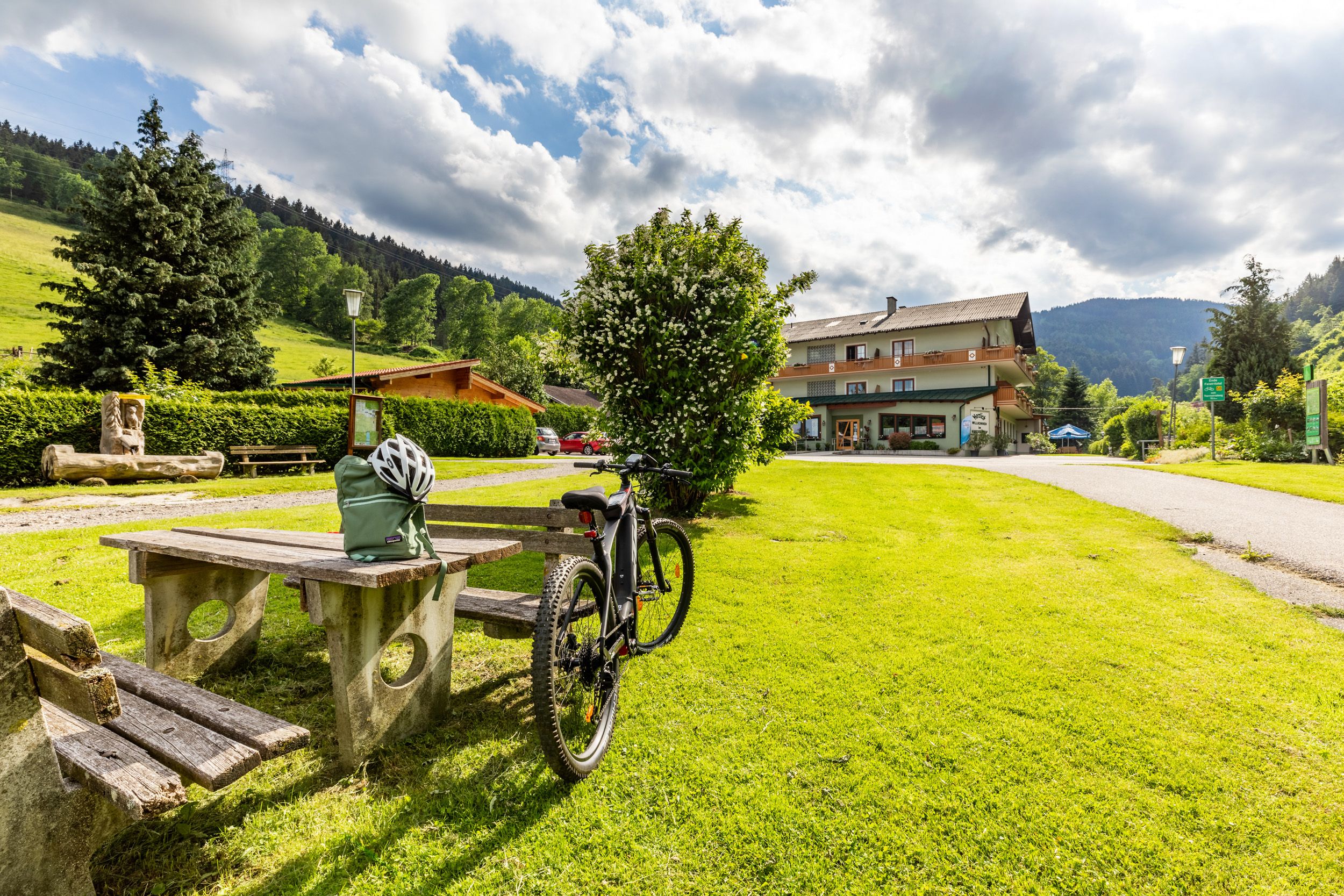 Ein Fahrrad steht neben einem Picknicktisch auf einer grünen Wiese vor einem Gebäude namens Hubertushof.