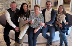 Fünf Personen sitzen auf einer Bank, drei Personen davon halten einen Becher in den Händen.