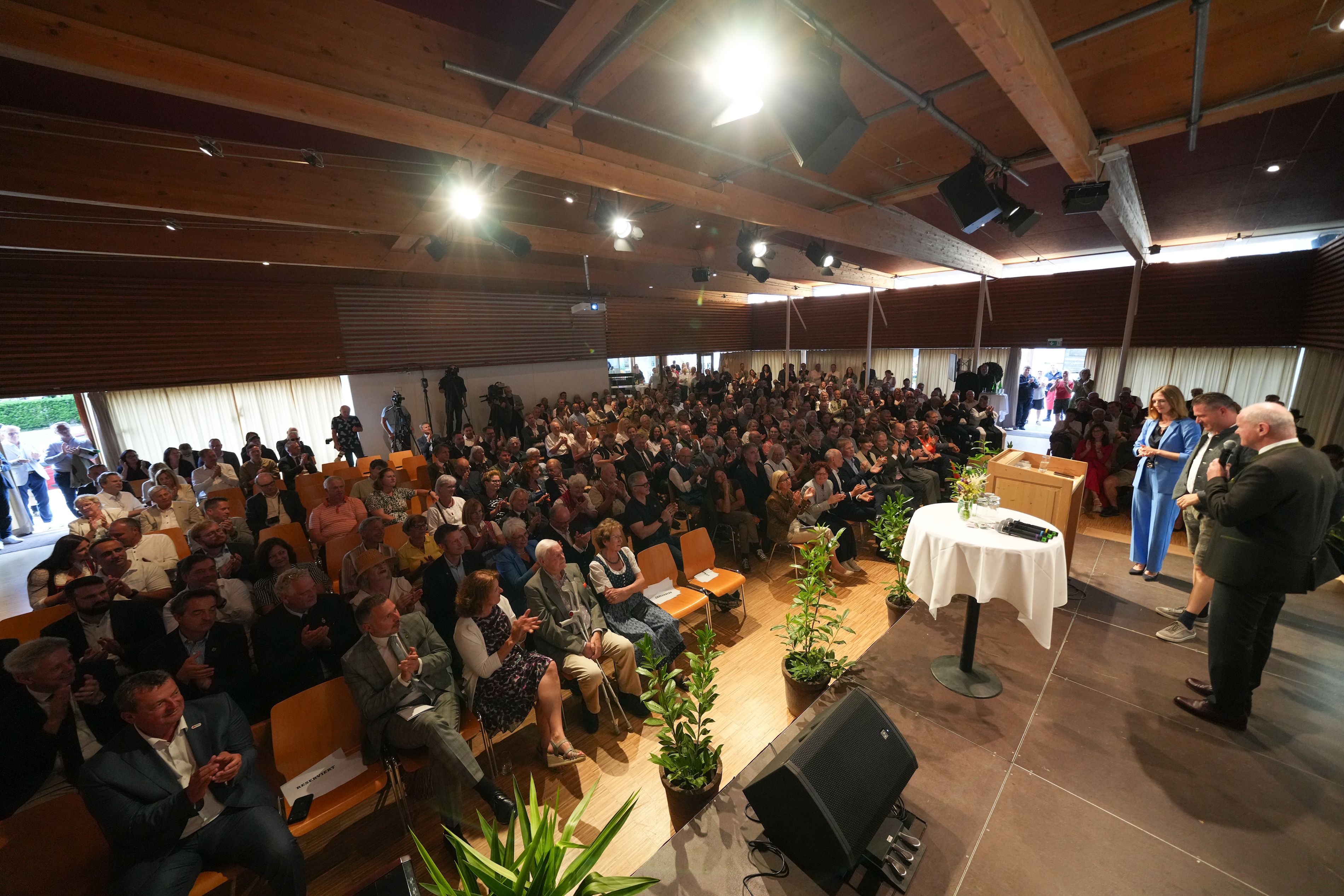 Blick von einer Bühne mit 3 Sprechern in einen voll besetzten Festsaal.