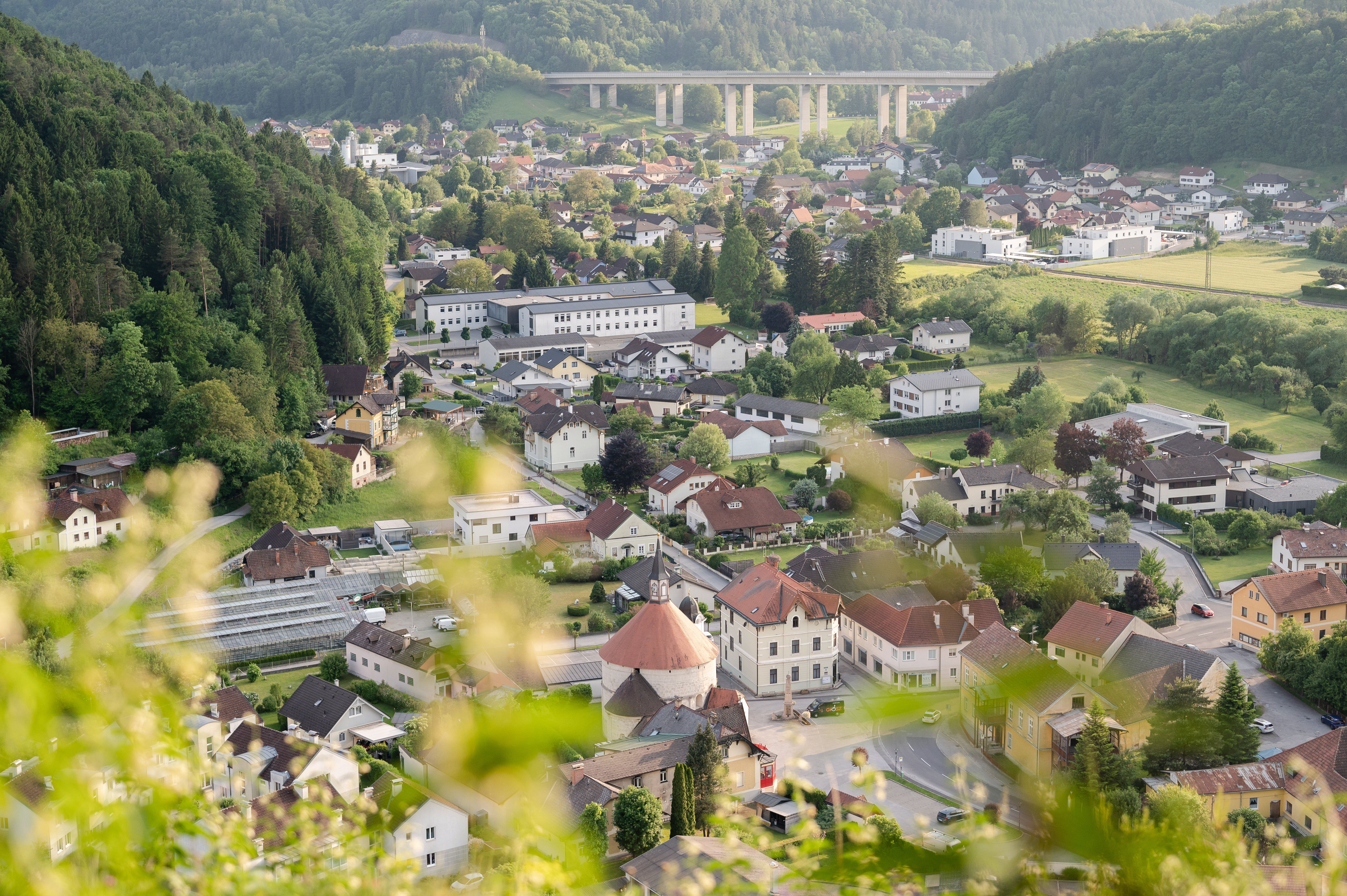 Blick auf den Ort Scheiblingkirchen-Thernberg mit umliegenden Hügeln und einer Autobahnbrücke im Hintergrund.