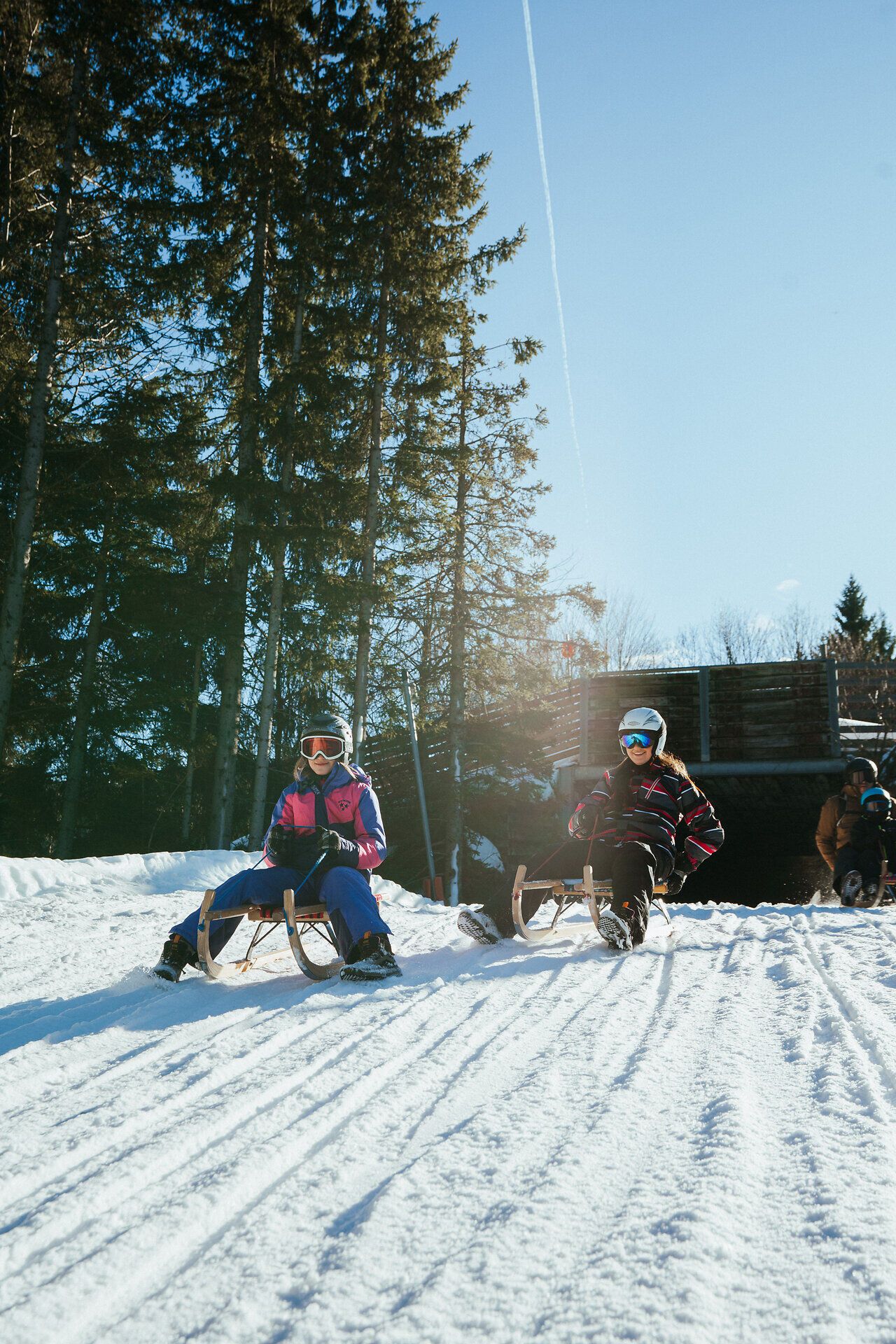 Zwei Personen beim Rodeln auf einer sonnigen, verschneiten Rodelbahn am Semmering Hirschenkogel.