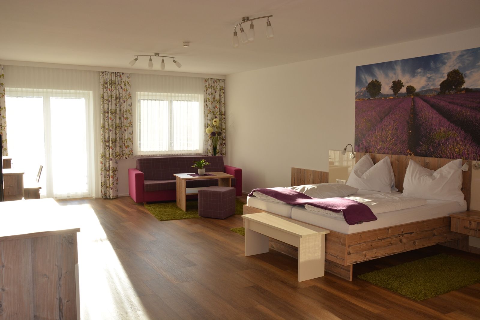 Ein modernes Doppelzimmer mit Holzboden, einem großen Bett, einer Sitzecke und einem Bild von Lavendelfeldern an der Wand.