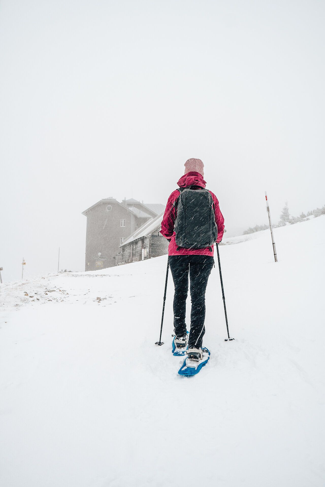 Inmitten einer winterlichen Landschaft, die von sanften Schneeverwehungen geprägt ist, wandert eine Person mit Schneeschuhen durch den frischen, glitzernden Schnee. Die schneebedeckten Hügel und die sanfte Stille der Umgebung schaffen eine friedliche Atmosphäre, die zum Entspannen und Genießen der Natur einlädt.