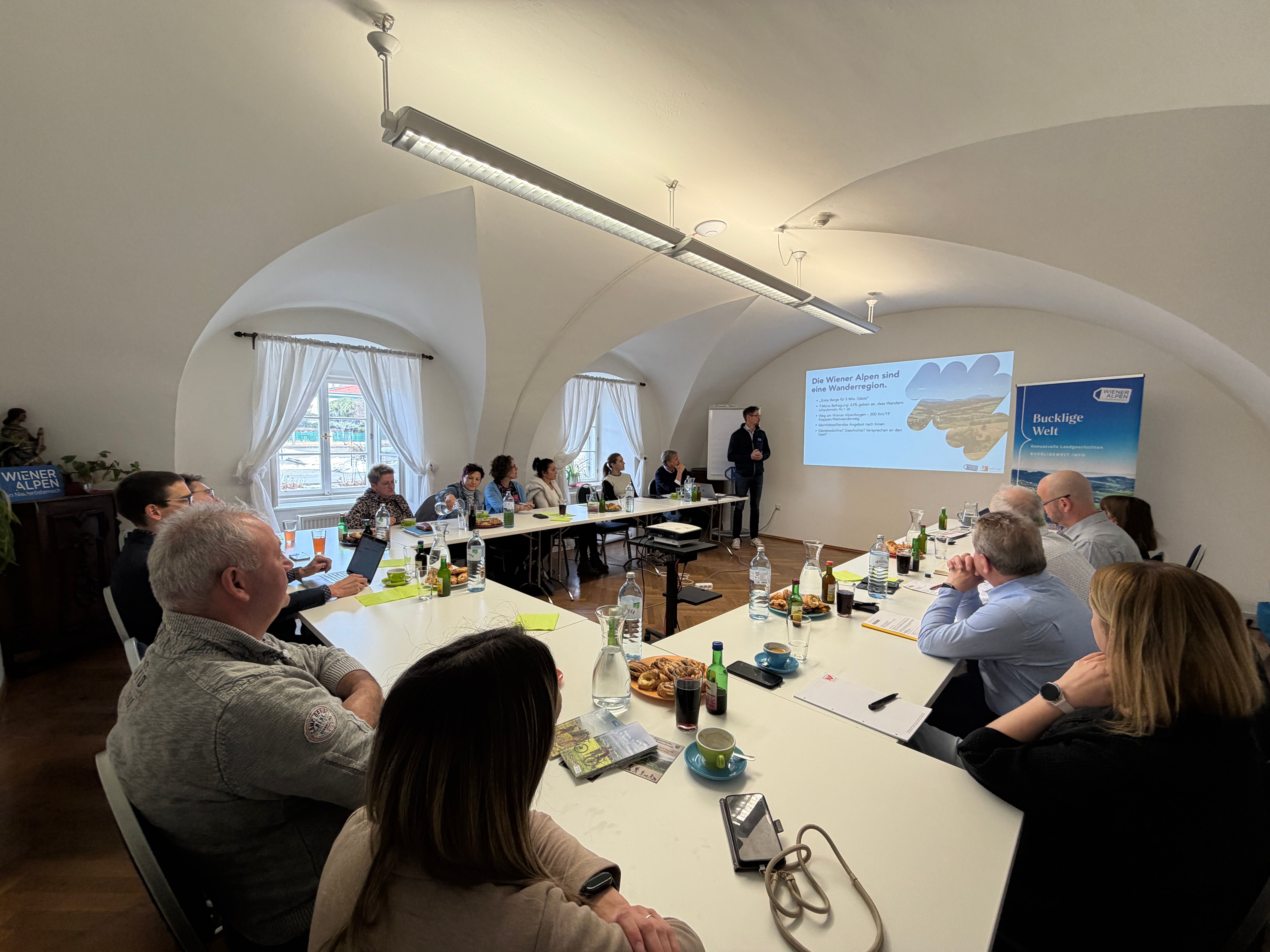 Workshop Teilnehmer sitzen an Tischen während ein Mann einen Vortrag hält.